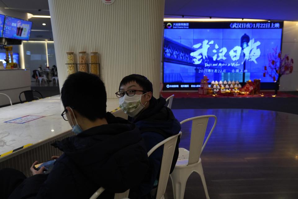 Youths wearing masks to protect from the coronavirus chat near a screen showing a trailer for the film "Days and Nights in Wuhan" in a cineplex in Wuhan in central China's Hubei province on Friday, Jan. 22, 2021. China is rolling out the state-backed film praising Wuhan ahead of the anniversary of the 76-day lockdown in the central Chinese city where the coronavirus was first detected. (AP Photo/Ng Han Guan)