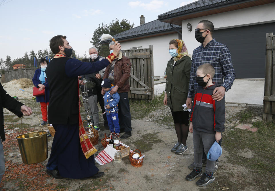 Priest of Ukrainian Orthodox Church Nazariy, wearing a face mask to protect against coronavirus, blesses family members near their house in the village of Nove close to capital Kyiv, Ukraine, Saturday, April, 18, 2020. All the Ukrainian churches have been closed for people because of COVID-19 outbreak, and believers wait for the priest near their houses. For Orthodox Christians, this is normally a time of reflection, communal mourning and joyful release, of centuries-old ceremonies steeped in symbolism and tradition. But this year, Easter - by far the most significant religious holiday for the world's roughly 300 million Orthodox - has essentially been cancelled. (AP Photo/Efrem Lukatsky)