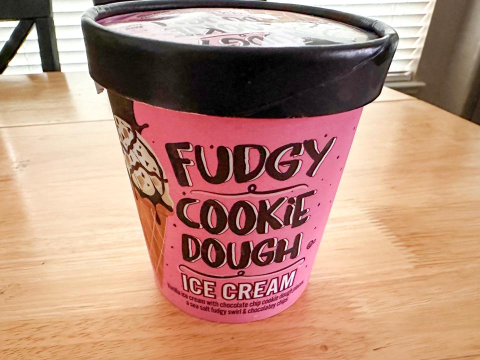 A pink tub of ice cream with a brown lid and brown "fudgy cookie dough" and white "ice cream" text