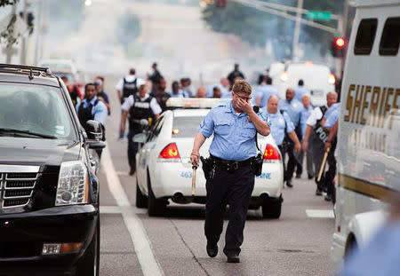 A policeman rubs his eyes after police attempted to disperse a crowd using what appeared to be teargas after a shooting incident in St. Louis, Missouri August 19, 2015. REUTERS/Kenny Bahr