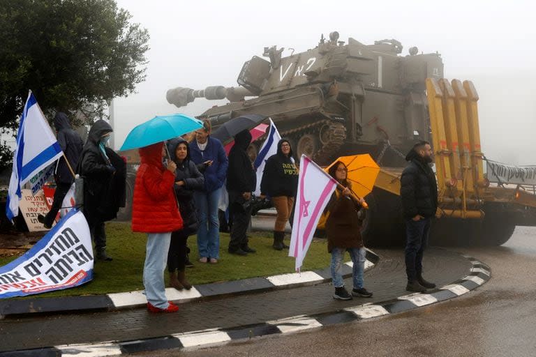 Un camión cargado con un tanque del ejército pasa junto a manifestantes israelíes que participan en una manifestación antigubernamental frente a la escuela Ramat Chorazim en Moshav Elifelet, en el norte de Israel, el 23 de enero de 2024.