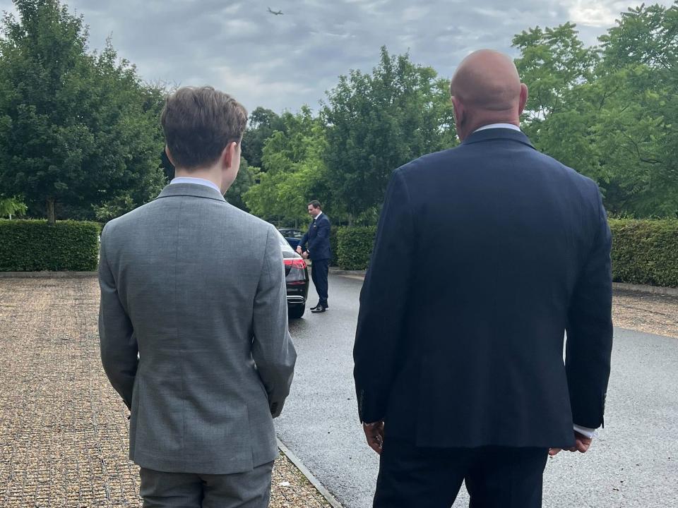 A shorter man in a grey suit and a tall bald man in a navy suit walk side-by-side as viewed from behind.