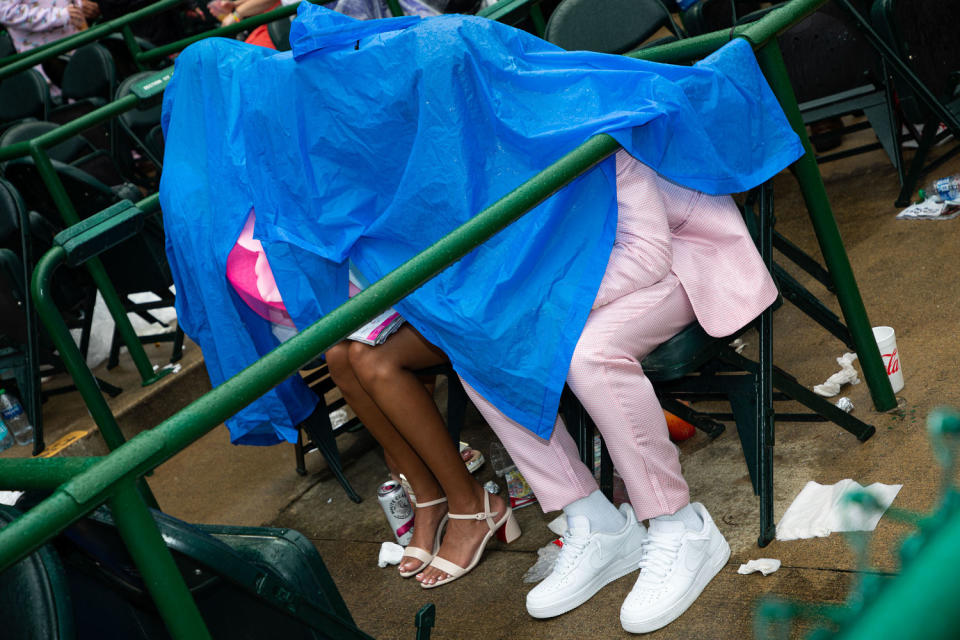 Attendees cover themseles in a blue plastic tarp. Their heels and sneakers peek out beneath.