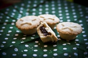 Four Christmas mince pies, One half eaten, on a green and white spotted napkin.