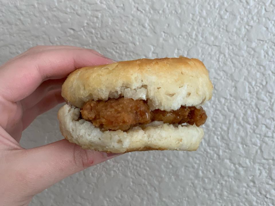 Hand holding Wendy's honey butter chicken biscuit in front of white wall