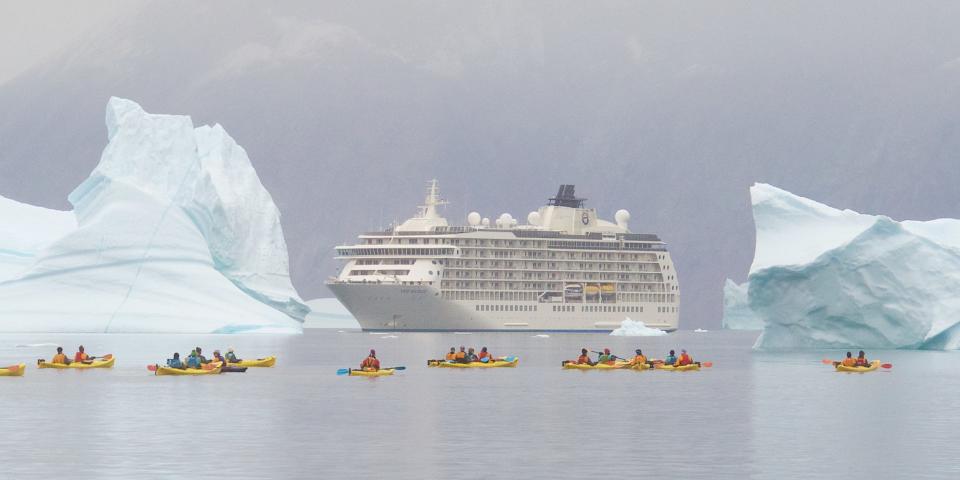 The World sailing on water by kayakers who are weaving through large icebergs.