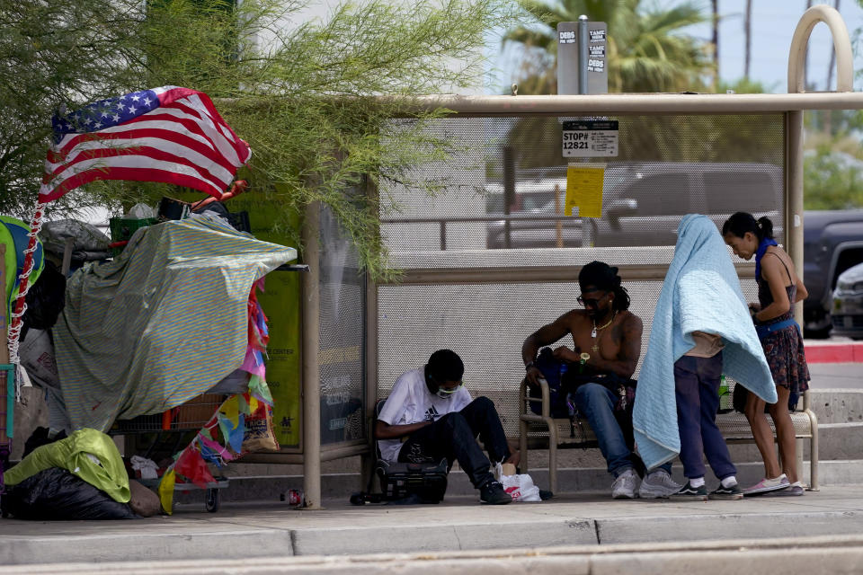 People gather under the shade of a bus stop, Tuesday, July 11, 2023 in Phoenix. Even desert residents accustomed to scorching summers are feeling the grip of an extreme heat wave smacking the Southwest this week. Arizona, Nevada, New Mexico and Southern California are getting hit with 100-degree-plus Fahrenheit temps and excessive heat warnings. (AP Photo/Matt York)