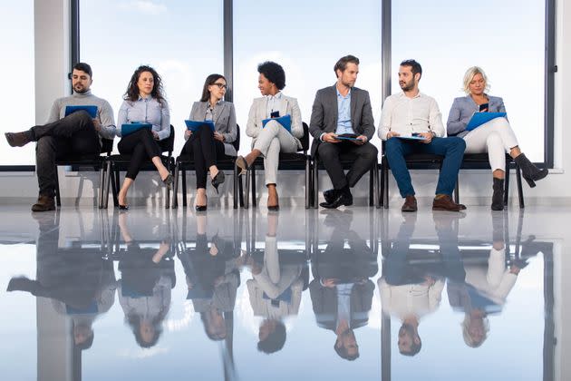 Large group of entrepreneurs sitting on chairs in waiting room before their job interview. Their reflection is seen in floor. Copy space. (Photo: skynesher via Getty Images)