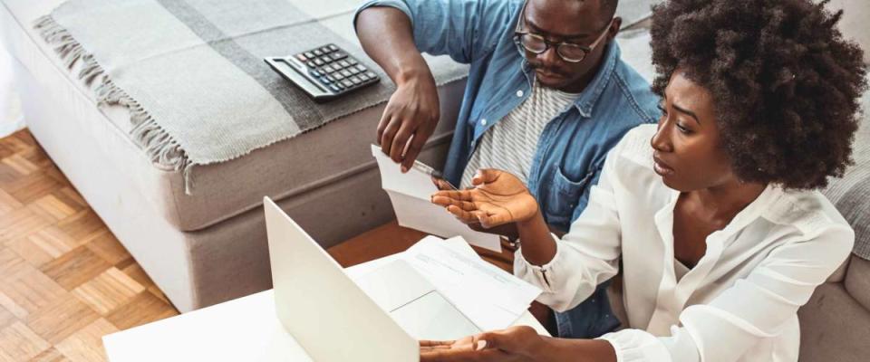 Desperate couple doing their accounts in the living room. Serious African American couple discussing paper documents, sitting together on couch at home, man and woman checking bills