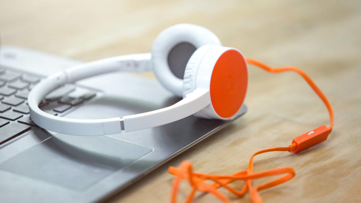  A photograph of a wired set of headphones, resting on top of an open, silver metal coloured laptop, on a light wood desk. 