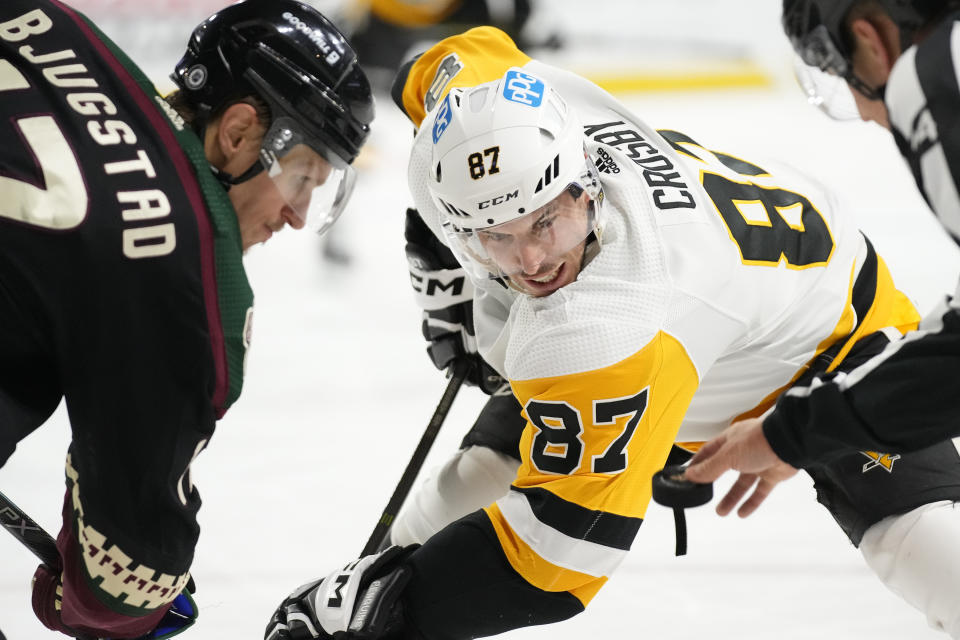 Pittsburgh Penguins center Sidney Crosby (87) watches the puck as linesman Trent Knorr, right, drops the puck on a face off against Arizona Coyotes center Nick Bjugstad, left, during the second period of an NHL hockey game in Tempe, Ariz., Sunday, Jan. 8, 2023. (AP Photo/Ross D. Franklin)