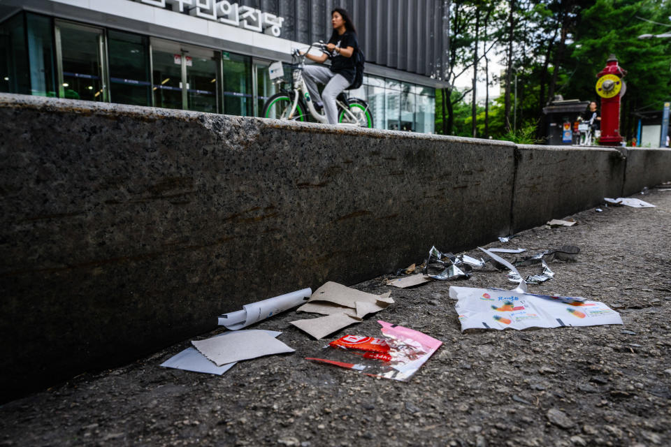 A woman cycles down a sidewalk past pieces of North Korean food packaging, sweet wrappers and paper suspected to be from trash balloons sent from North Korea, in Seoul, South Korea, July 24, 2024. / Credit: ANTHONY WALLACE/AFP/Getty