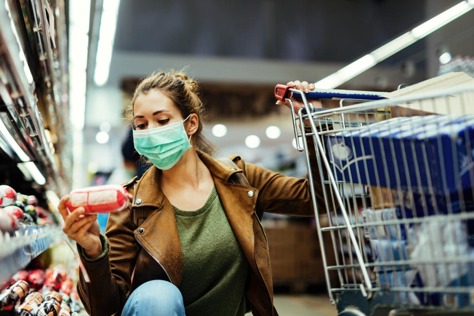 Young woman wearing protective mask and buying food in grocery store during coronavirus pandemic.