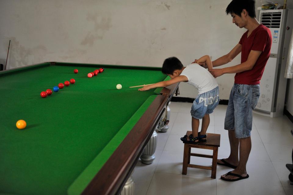 Three-year-old Wang Wuka plays a shot as his father Wang Yin steadies his arm during snooker practice at their home in Xuancheng