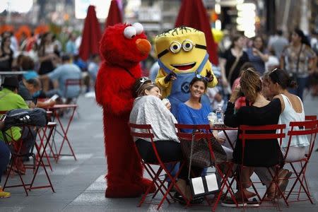 Jorge, an immigrant from Mexico, poses with women while dressed as the Sesame Street character Elmo in Times Square, New York July 30, 2014. REUTERS/Eduardo Munoz