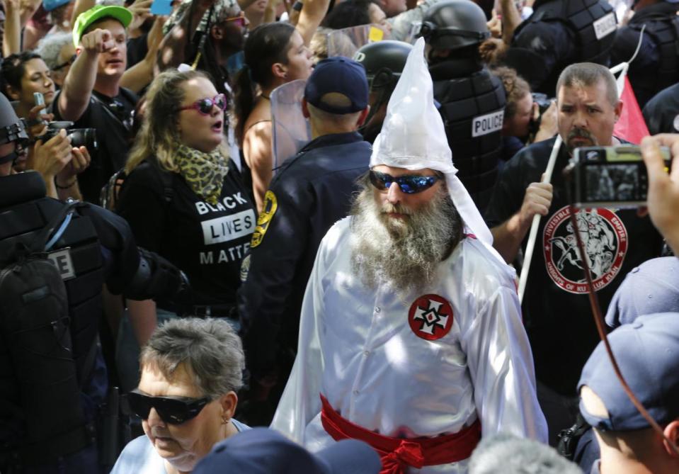 Members of the KKK are escorted by police past a large group of protesters during a rally in Charlottesville (AP)