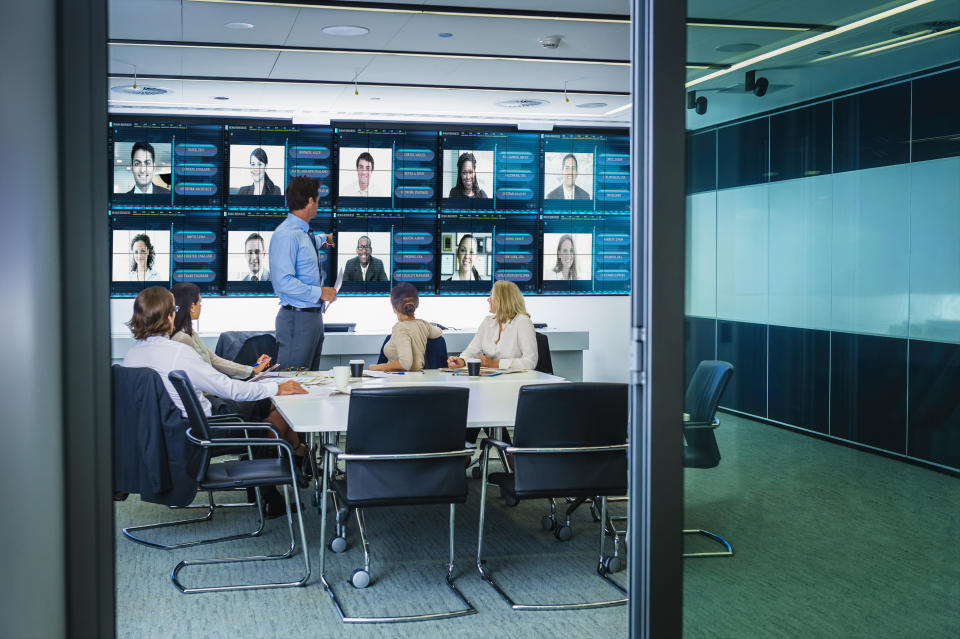 People sit in an office meeting room, while other employees can be seen on video screens. (Source: Getty)