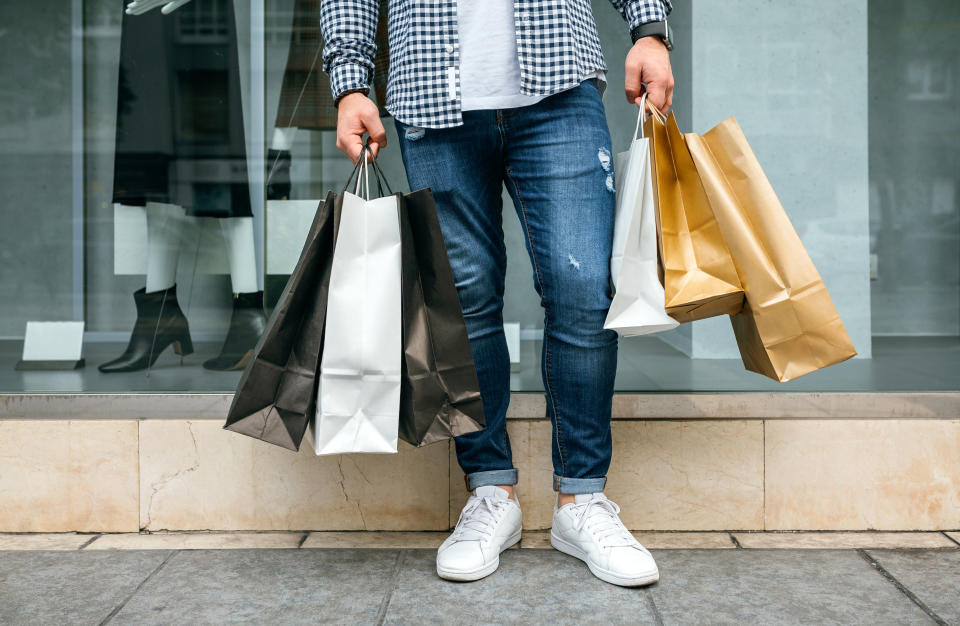 Low Section Of Young Man Holding Shopping Bags While Standing On Sidewalk