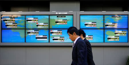 Men walk past an electronic board showing Japan's Nikkei average outside a brokerage in Tokyo, Japan, November 18, 2016. REUTERS/Toru Hanai