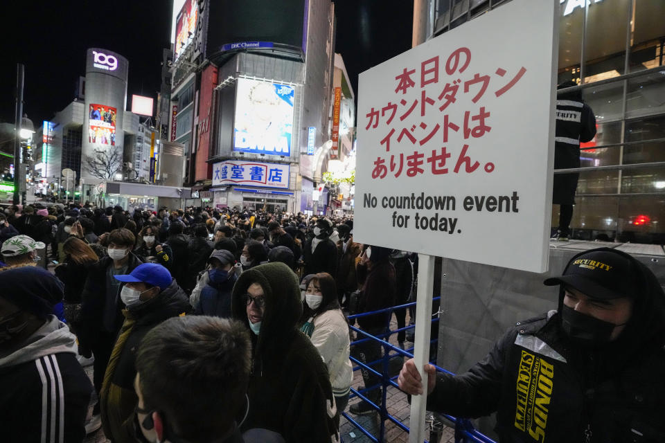 A security guard holds up a sign indicating that there is no countdown event at the famed Shibuya scramble crossing, a popular location for New Year's Eve gathering Friday, Dec. 31, 2021, in Tokyo as people gather to celebrate New Year's eve. (AP Photo/Kiichiro Sato)