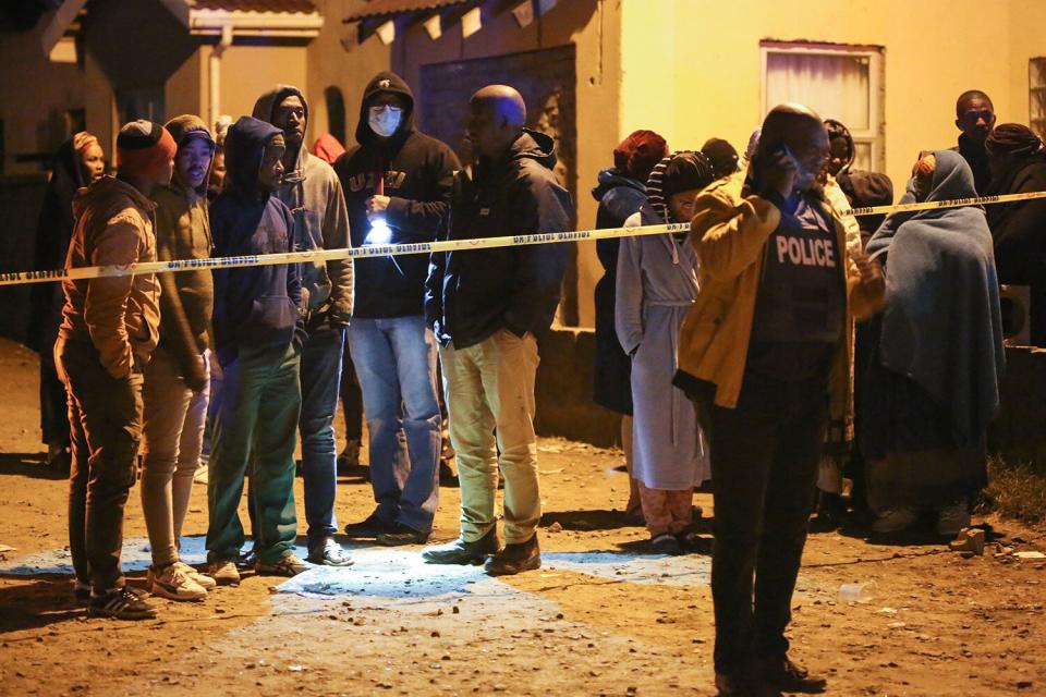 Members of the community and family wait for news outside a township pub as a police officer talks on a phone in South Africa's southern city of East London