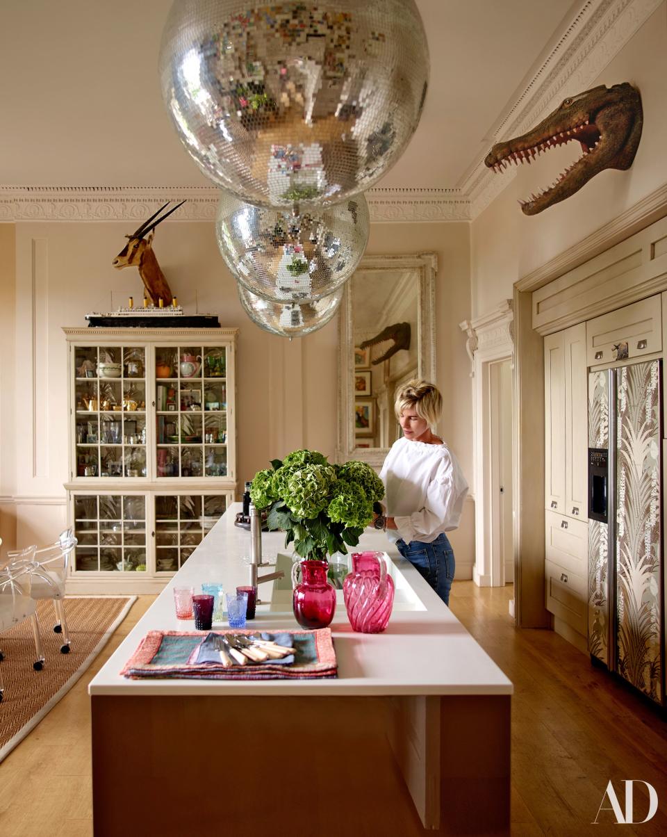 Brooke arranges hydrangeas on the Boffi kitchen island beneath disco balls. A model of the Titanic sits atop the cabinet; Florence Broadhurst wallpaper covers the refrigerator doors.