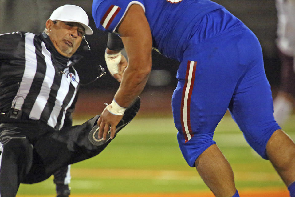 Football referee Fred Gracia falls to the turf after being charged by Edinburg's Emmanuel Duron in Edinburg's high school zone play-in game against Pharr-San Juan-Alamo on Thursday, Dec. 3, 2020, in Edinburg, Texas. Duron was escorted from the stadium by police officers. (Joel Martinez/The Monitor via AP)