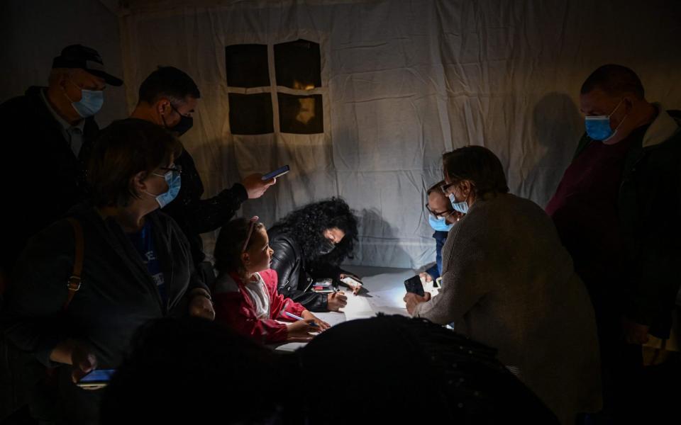 People inside a tent use mobile phones' light to fill-in forms prior being vaccinated during the vaccination marathon - Daniel MIHAILESCU / AFP