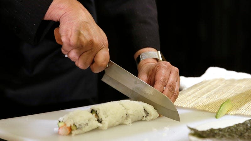 A sushi roll gets sliced by someone holding a knife