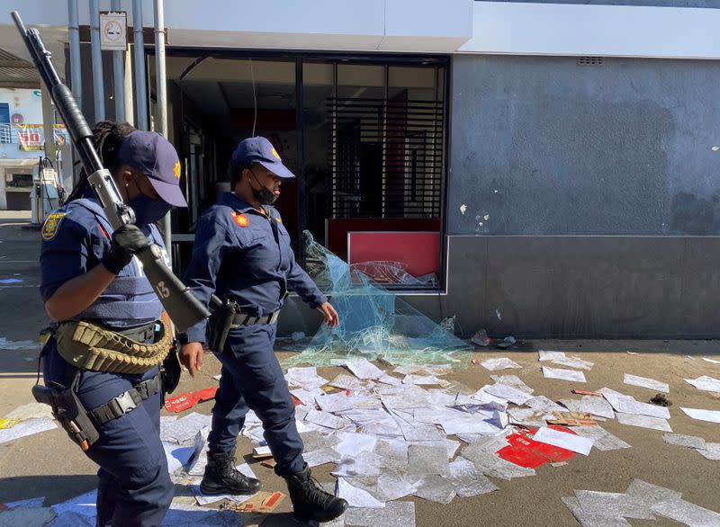 Police walk past a shop looted in protests following the jailing of former South African President Jacob Zuma, in Durban