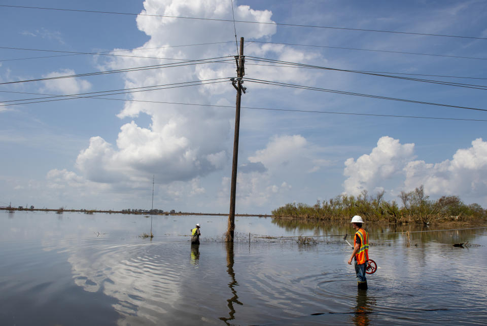 Utility crews stand in water as they work on repairing power lines along Highway 23 in Plaquemines Parish, La., over a week after Hurricane Ida on Tuesday, Sept. 7, 2021. (Chris Granger/The Times-Picayune/The New Orleans Advocate via AP)