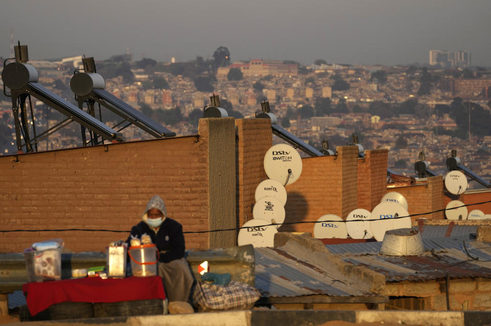 FILE - A woman selling fat cakes sits in front of low-cost housing with solar geysers and cable TV dishes in the Alexandra township of Johannesburg, South Africa, Aug. 23, 2022. (AP Photo/Themba Hadebe, File)