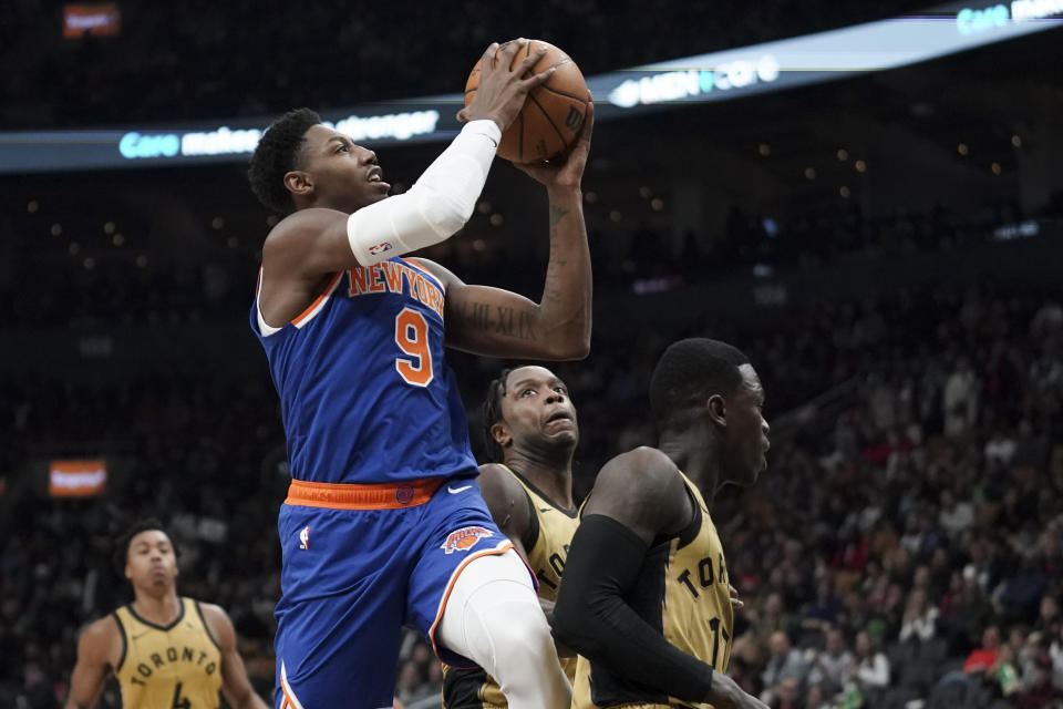 New York Knicks guard RJ Barrett (9) jumps past Toronto Raptors forward O.G. Anunoby, center, and guard Dennis Schroder, right, during second-half NBA basketball game action in Toronto, Friday, Dec. 1, 2023. (Arlyn McAdorey/The Canadian Press via AP)