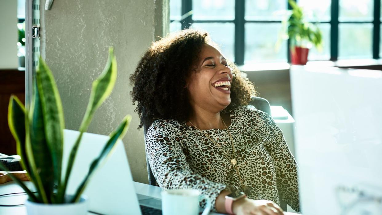 attractive businesswoman in animal print blouse, sitting at desk in modern office, head back, smiling and cheerful, eyes closed, curly hair, joy, carefree