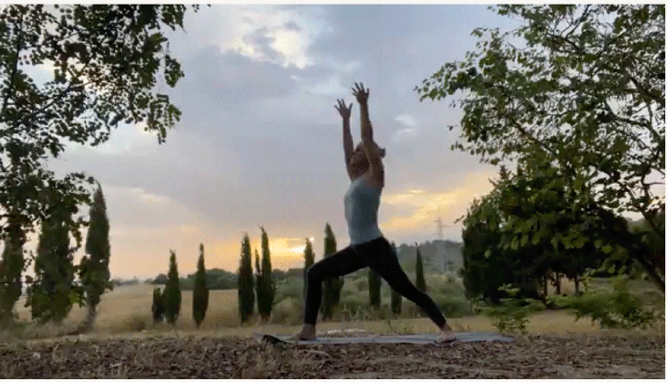 Woman outside practicing yoga at sunrise on her mat in Warrior 1