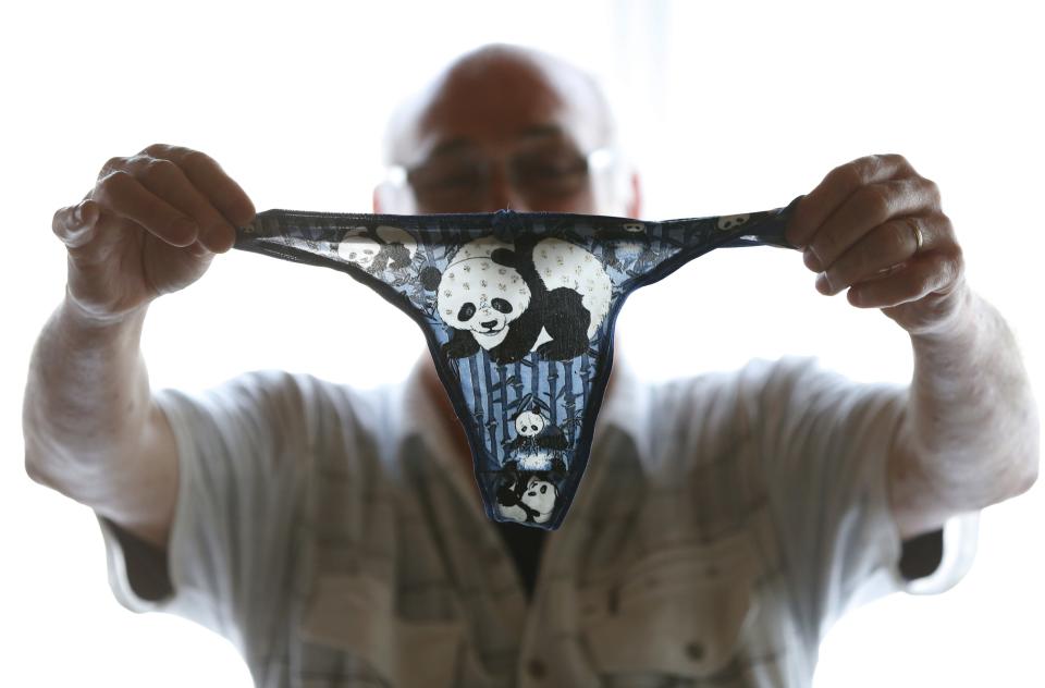 Andre Cornet holds a woman's underwear, part of a collection of about 2,200 pieces of panda collectables, in his house in Haccourt