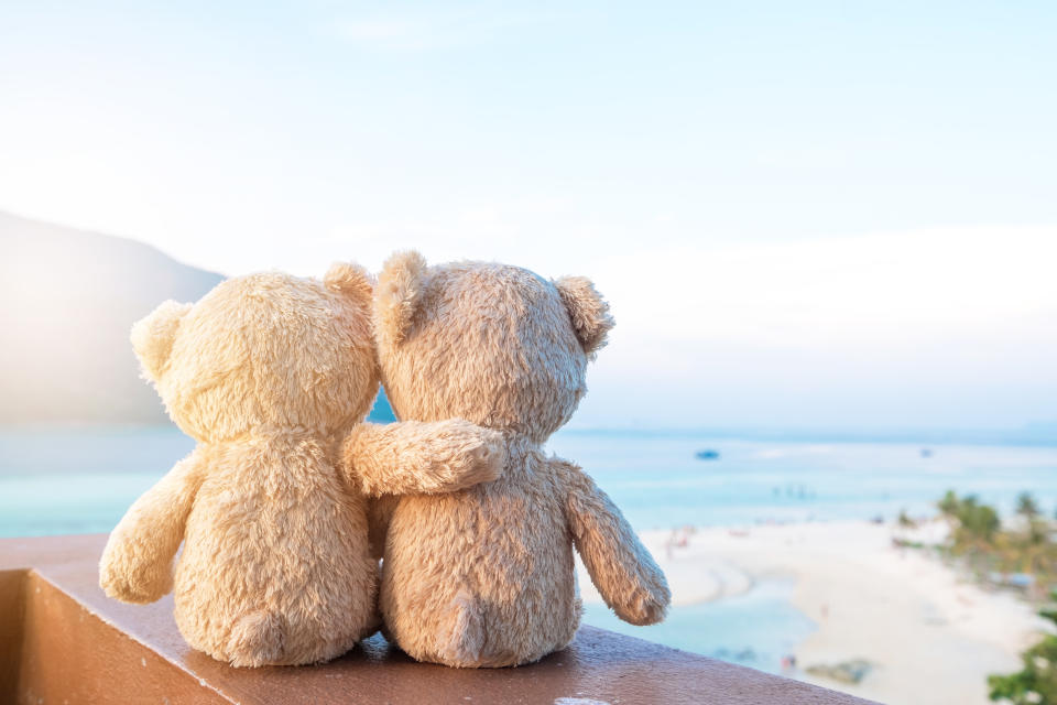 Two teddy bears sitting sea view. Love and relationship concept. Beautiful white sandy beach in the summer.