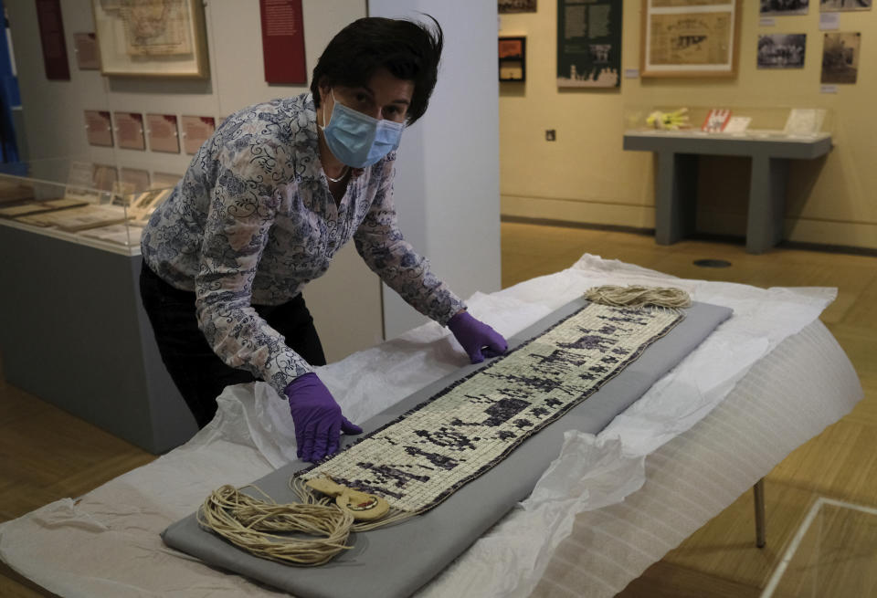 Co-curator Jo Loosemore looks up to the camera as she examines a recently created wampum belt made by members of the Wampanoag Native America people, after its unpacking and prior to it going on display in Southampton, England, Thursday, Aug. 13, 2020. On the 400th anniversary of the Mayflower voyage, commemorations are focusing on both the Pilgrim settlers and the Native people whose lives were transformed by their arrival. An exhibition in England focuses on one casualty of colonization: a wampum belt taken from the Wampanoag people to England in the 17th century, and then lost. (AP Photo/Alastair Grant)