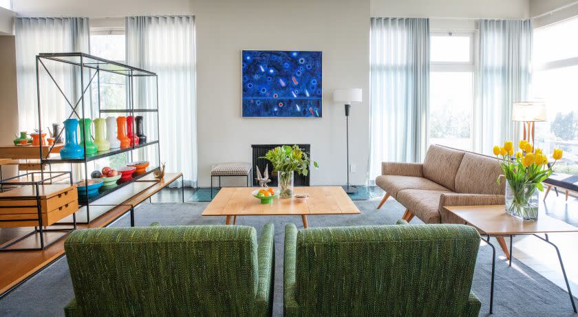 A view of a stylish living room with arm chairs with hairpin legs and a shelf room divider with colorful ceramics