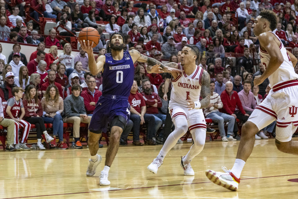 Northwestern guard Boo Buie (0) drives to the basket while being defended by Indiana guard Jalen Hood-Schifino (1) and forward Trayce Jackson-Davis, right, during the first half an NCAA college basketball game, Sunday, Jan. 8, 2023, in Bloomington, Ind. (AP Photo/Doug McSchooler)