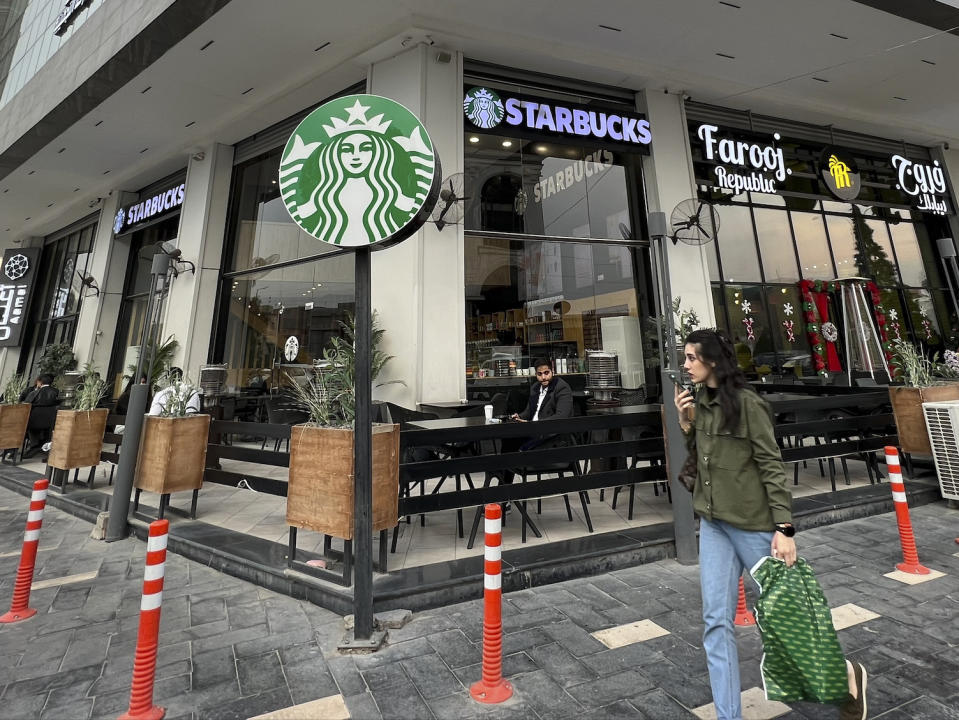 A woman walks by an unlicensed Starbucks cafe in Baghdad, Iraq, Wednesday, Dec. 21, 2022. Real Starbucks merchandise is imported from neighboring countries to stock the three cafes in the city, but all are unlicensed. Starbucks filed a lawsuit in an attempt to shut down the trademark violation but the case was shuttered after the owner allegedly threatened lawyers hired by the coffee house. (AP Photo/Ali Abdul Hassan)