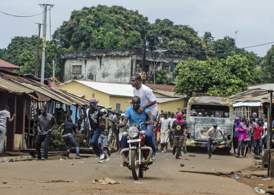 Men race away on a motorbike after throwing a dud grenade at pro-government protesters during pre-election violence in the Taouyah neighbourhood of Guinea's capital Conakry