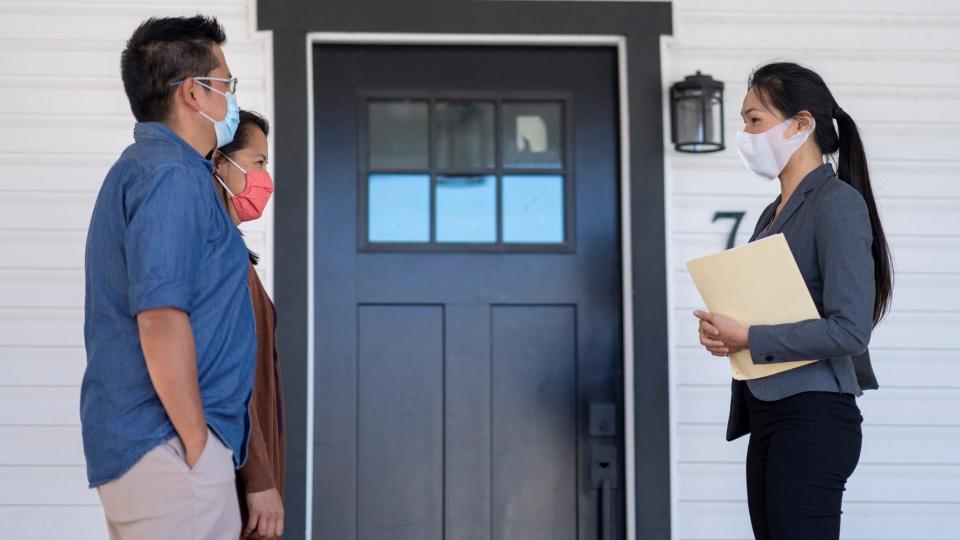 Female sales agent meeting with clients in front of a house for sale.