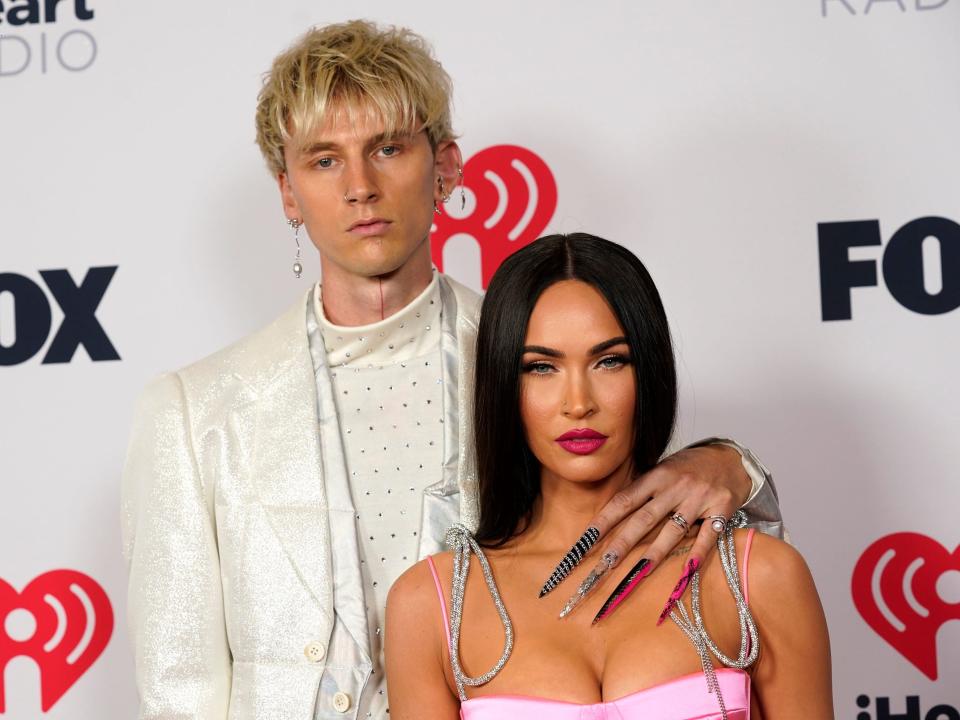 Machine Gun Kelly with his left arm around Megan Fox's shoulder at the red carpet of the 2021 iHeartRadio Music Awards.