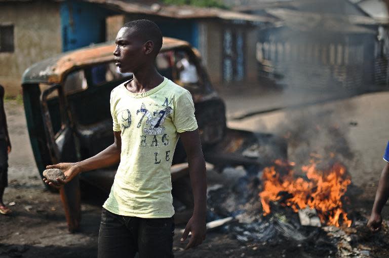 A protestor opposed to Burundian President Pierre Nkurunziza's third term brandishes a rock as he stands beside a burning vehicle during a demonstration in Bujumbura on May 26, 2015