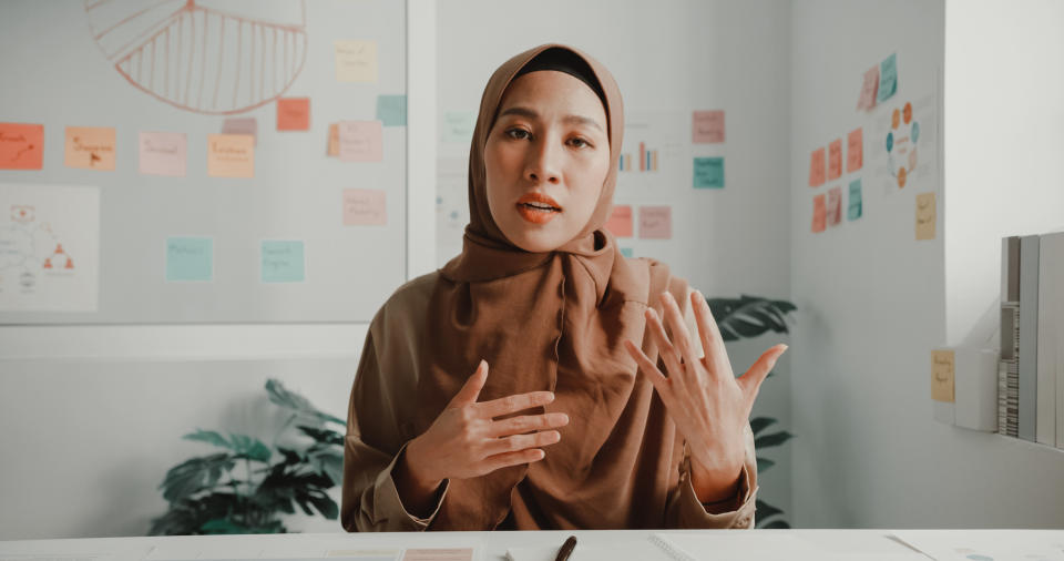 Woman in a hijab gesturing during a business presentation with sticky notes on wall behind her