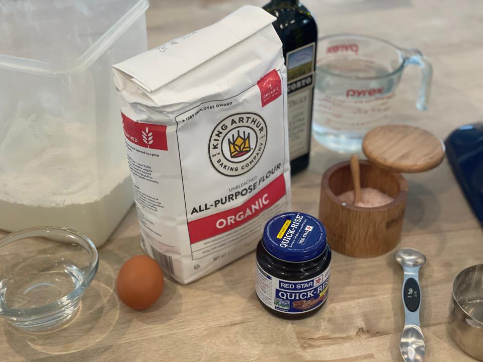 flour, yeast, salt, oil, and an egg on a counter for a bread recipe