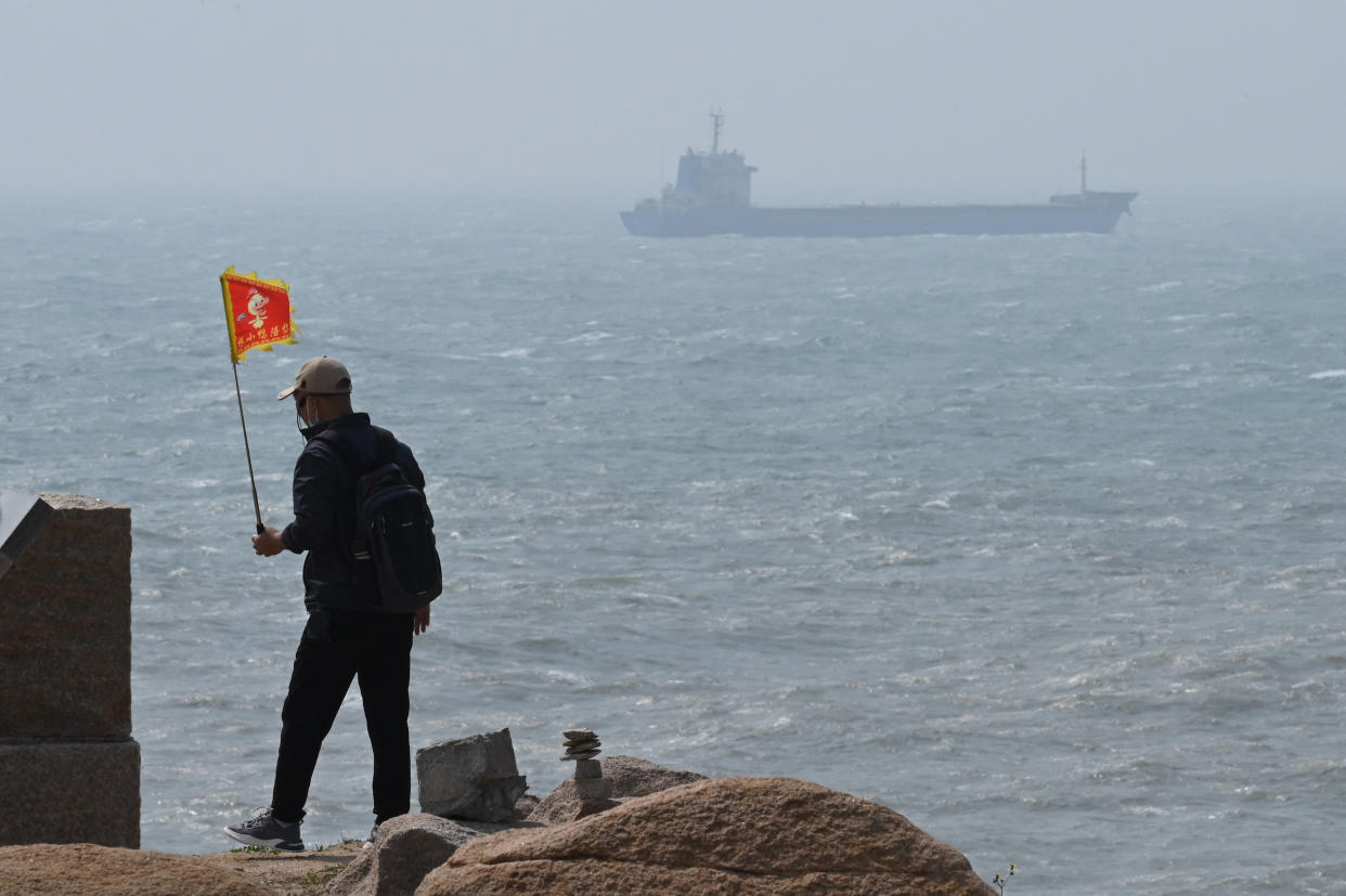 TOPSHOT - A man walks with a flag as a ship passes by behind him on Pingtan island, the closest point to Taiwan, in Chinas southeast Fujian province on April 8, 2023. - China launched military drills around Taiwan on April 8, in what it called a 