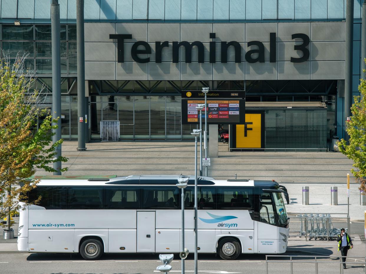 A bus used to transport red list arriving airline passengers passes Heathrow Terminal 3 building at Heathrow Airport