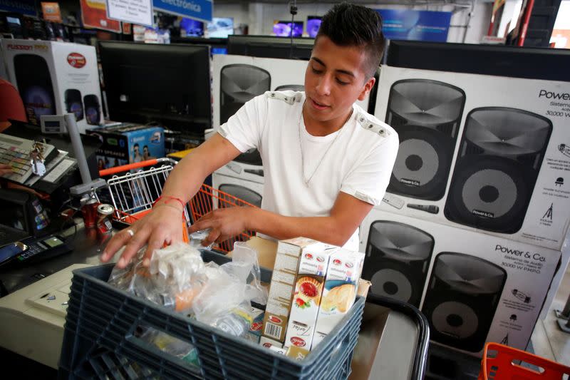 A man arranges groceries in a plastic box at a supermarket which no longer provides plastic bags for customers to carry products, in Mexico City